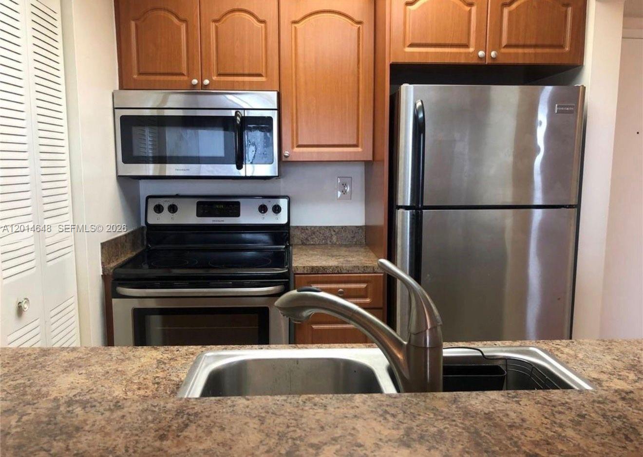 A kitchen features wood cabinets, stainless steel appliances, and a granite countertop with a sink — 800 N Miami Ave # 407, Miami FL 33136, MIAMI, FL
