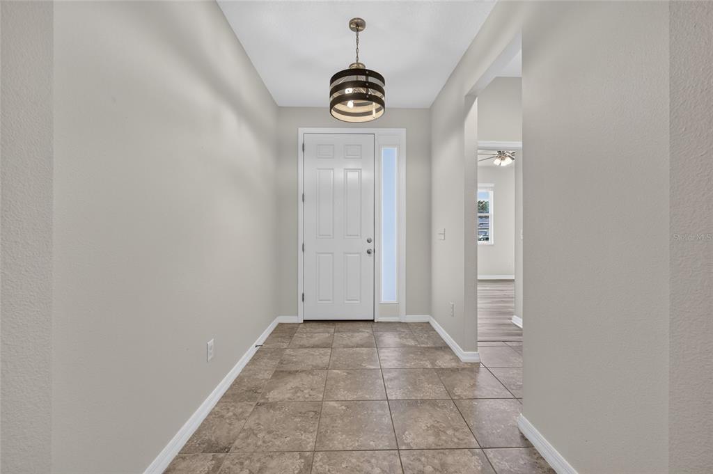 A foyer with tiled flooring, a white front door, and a modern drum pendant light — 5601 SW 50TH AVENUE, OCALA, FL