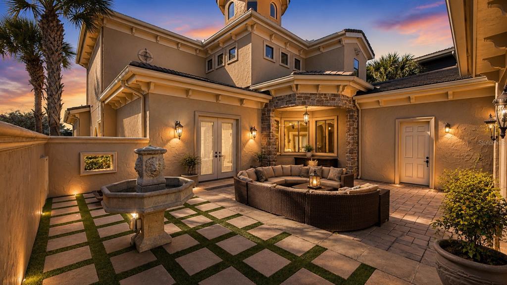 A stone-paved patio features a tiered fountain, a curved wicker sofa, and a house exterior — 340 MUIRFIELD LOOP, REUNION, FL