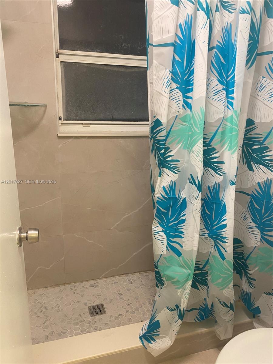 A tiled walk-in shower features a window and a blue and white leaf-patterned curtain — 2953 SE 15th Ter, Homestead FL 33035, HOMESTEAD, FL