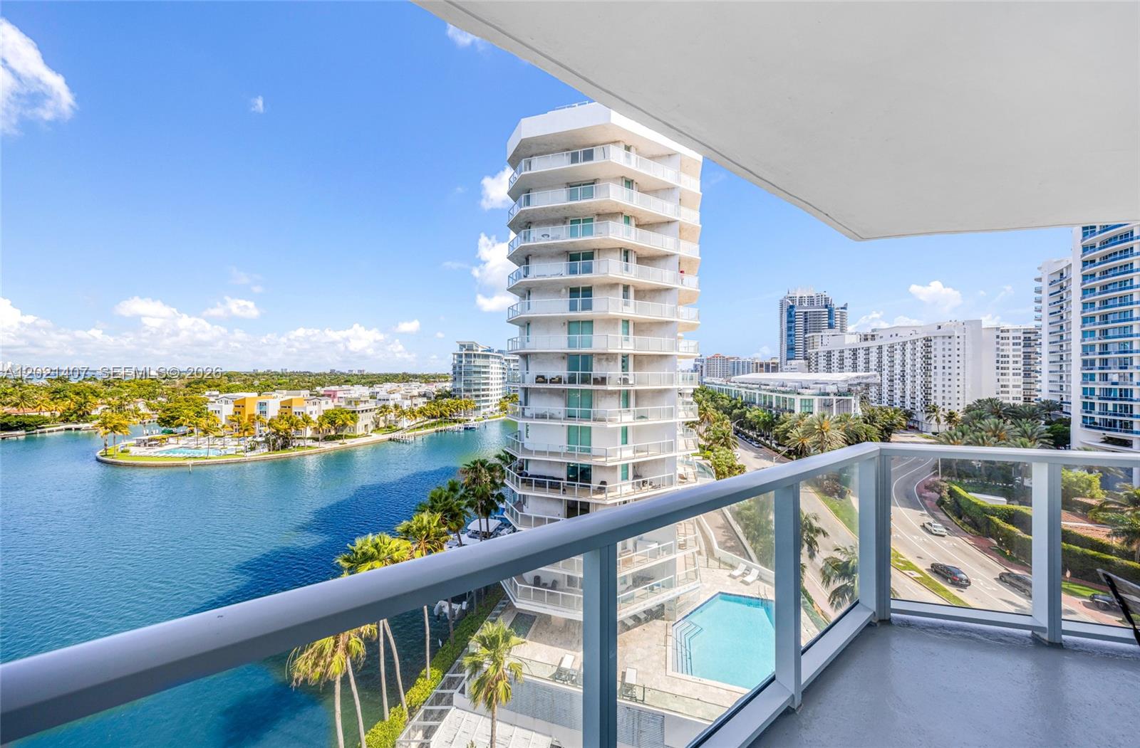 A balcony view overlooks a canal, a tall residential building, and a swimming pool — 5880 Collins Ave # 1007, Miami Beach FL 33140, MIAMI BEACH, FL