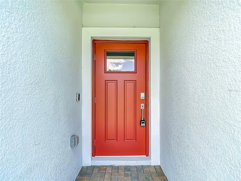 A bright orange front door with a small window is set within a white entryway — 6799 HOMEBOUND WAY, NEW PORT RICHEY, FL