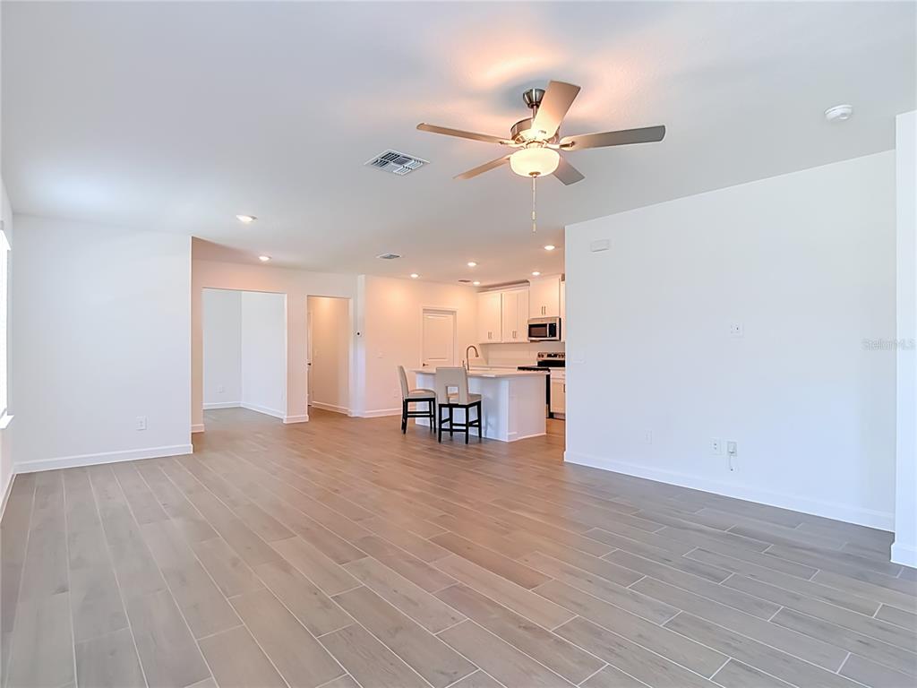 An open-concept living area features light wood-look tile flooring, white walls, and a kitchen island — 6799 HOMEBOUND WAY, NEW PORT RICHEY, FL