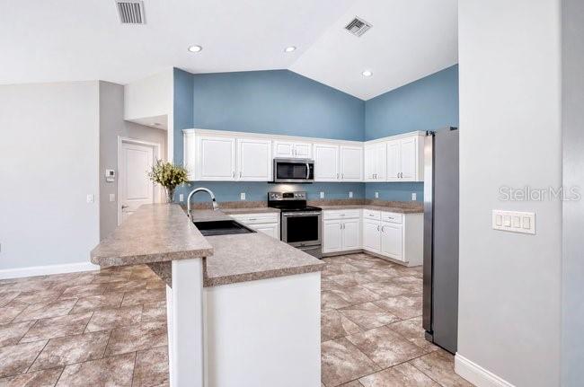 A kitchen features white cabinets, blue walls, a breakfast bar, and brown tile flooring — 3975 SUNNYWOOD CIRCLE, LAKELAND, FL