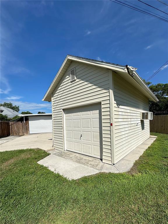 A detached garage with light-colored siding and a white roll-up door stands on grass — 606 NEW YORK AVE UNIT New York Ave, ST CLOUD, FL