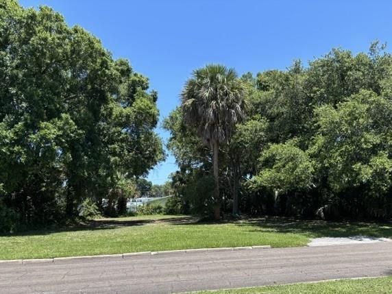 A vacant, grassy residential lot is bordered by mature trees and a paved street — VERO BEACH, FL