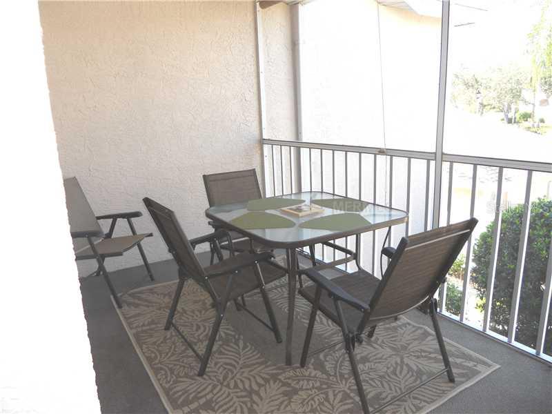 A screened-in balcony features a glass-top dining table with four chairs and a patterned rug — 8911 VERANDA WAY UNIT 222, SARASOTA, FL
