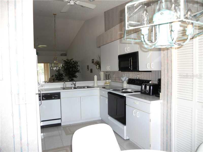 A kitchen features white cabinets, black appliances, a double sink, and a breakfast bar — 8911 VERANDA WAY UNIT 222, SARASOTA, FL