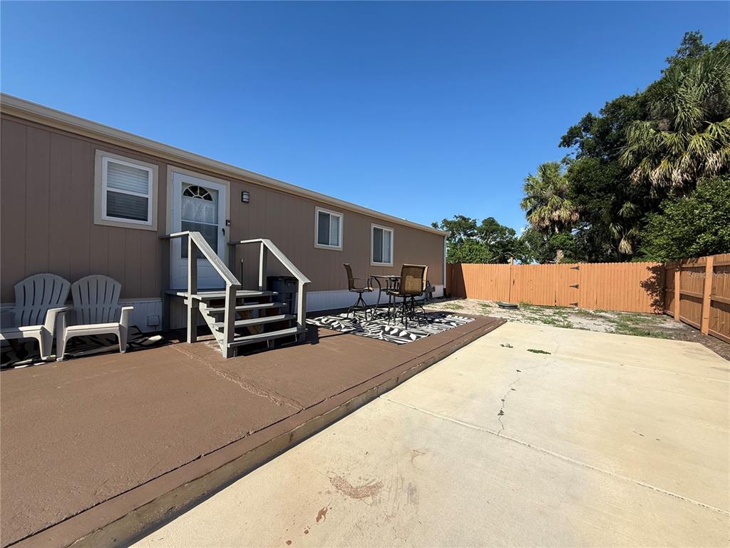 A mobile home exterior features a concrete patio, wooden steps, and a fenced backyard — 8438 FORMEL AVENUE, PORT RICHEY, FL