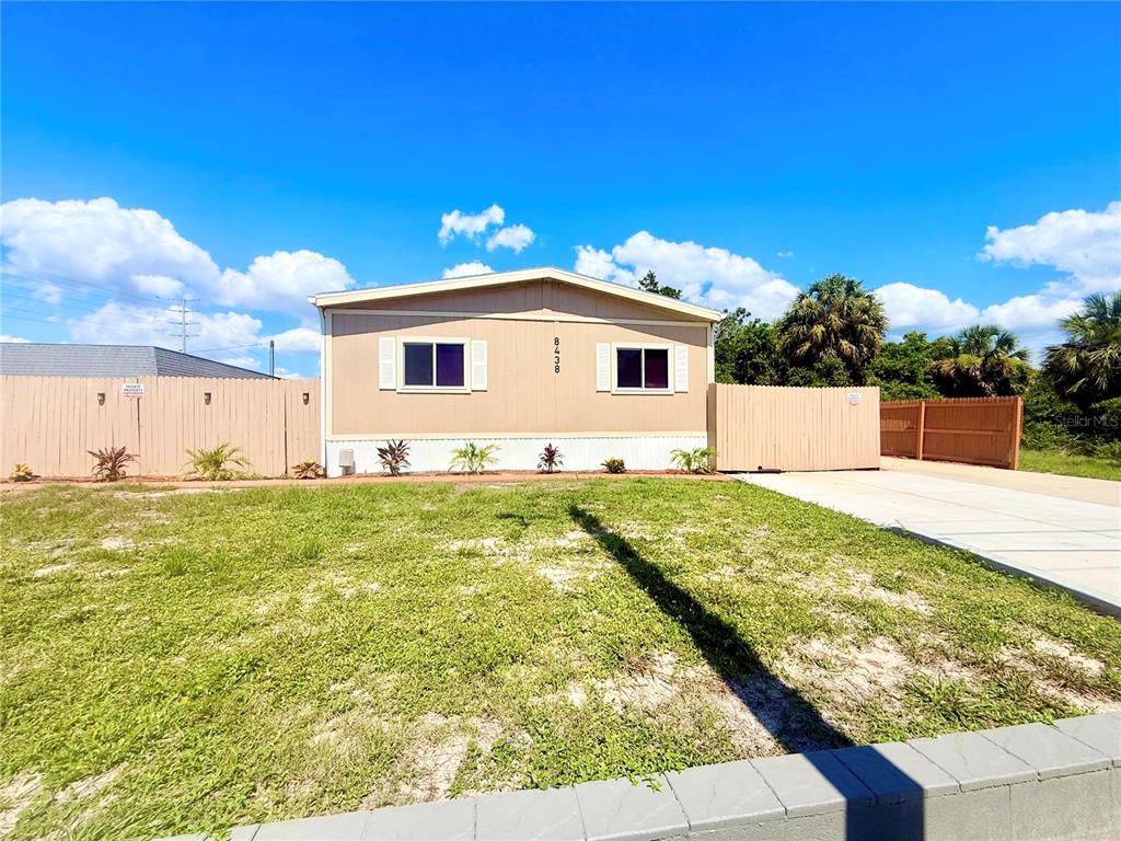 A tan single-story manufactured home with a concrete driveway and a wooden privacy fence — 8438 FORMEL AVENUE, PORT RICHEY, FL