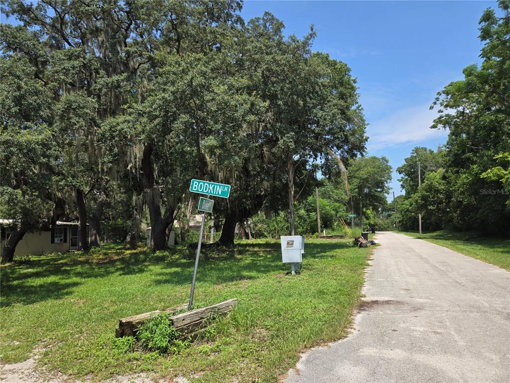 A street sign for Bodkin Lane stands near a gravel road lined with large trees — 1665 BODKIN LANE, OVIEDO, FL