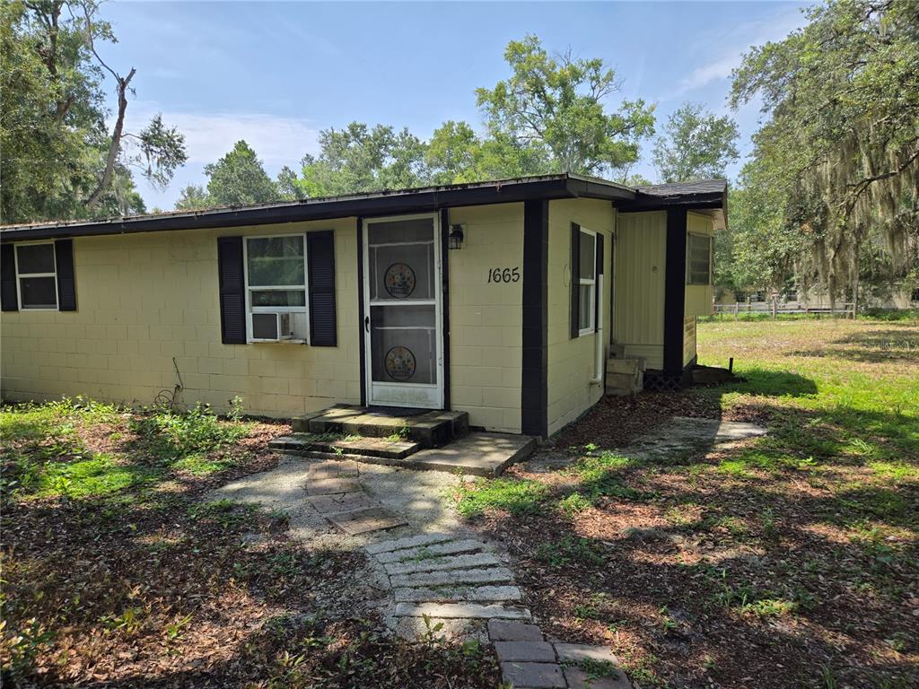 A single-story house with yellow block walls, black trim, and a screen door entrance — 1665 BODKIN LANE, OVIEDO, FL