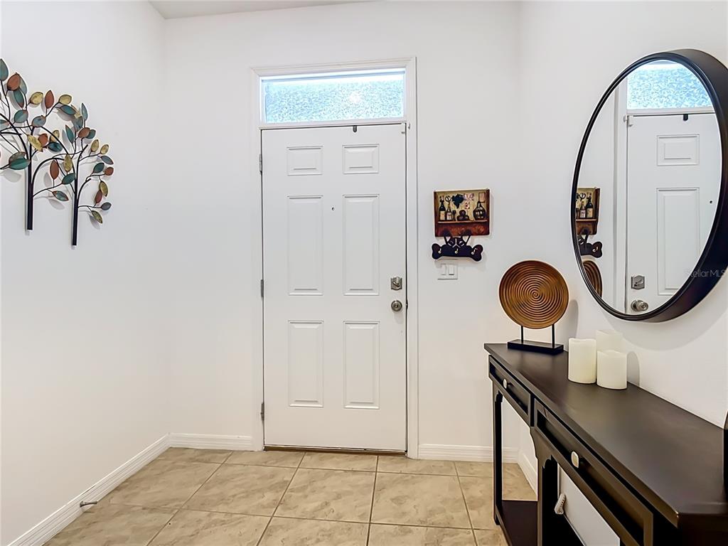 An entryway features a white door, a dark console table, a round mirror, and wall art — 1229 YELLOW FINCH DRIVE, DAVENPORT, FL