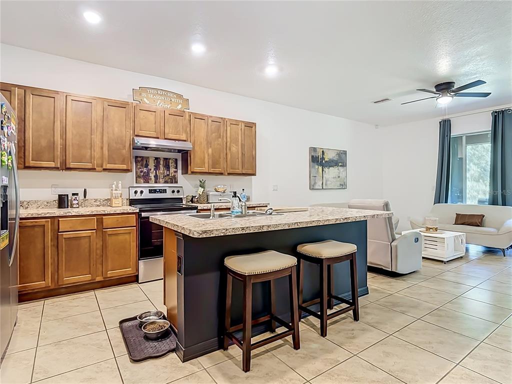 A kitchen with wooden cabinets and a dark island features a breakfast bar with stools — 1229 YELLOW FINCH DRIVE, DAVENPORT, FL