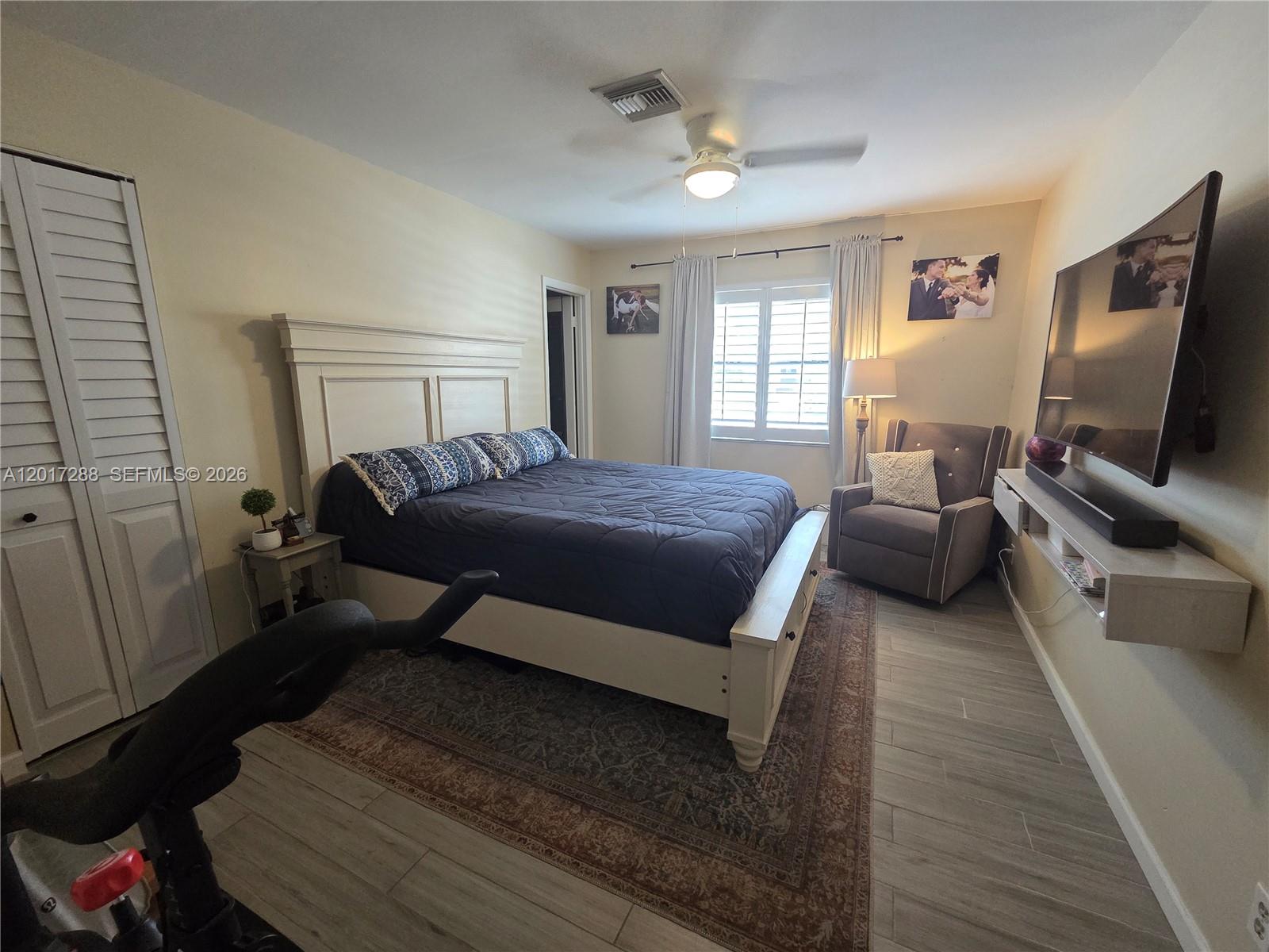 A bedroom features a white bed frame, a dark blue comforter, and a wall-mounted television — 19 Chestnut Cir, Cooper City FL 33026, COOPER CITY, FL