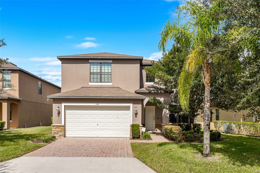 A two-story suburban house features a tan stucco exterior, a two-car garage, and a palm tree — 1144 CYPRESS POINTE BOULEVARD, DAVENPORT, FL
