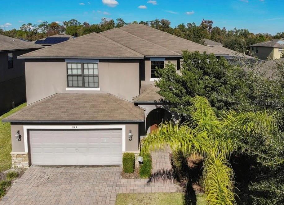 A two-story suburban house with a tan stucco exterior, a two-car garage, and a palm tree — 1144 CYPRESS POINTE BOULEVARD, DAVENPORT, FL