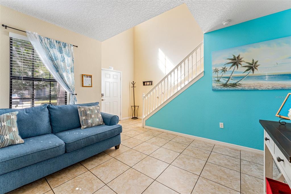 A living room features a blue sofa, tiled floors, a staircase, and a turquoise accent wall — 1144 CYPRESS POINTE BOULEVARD, DAVENPORT, FL