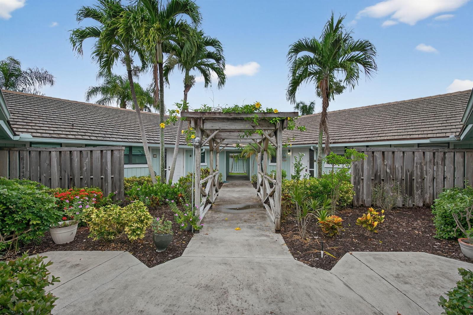 A wooden pergola spans a concrete walkway leading to the entrance of a residential building — 1127 E Seminole Avenue # 8a, Jupiter FL 33477, JUPITER, FL