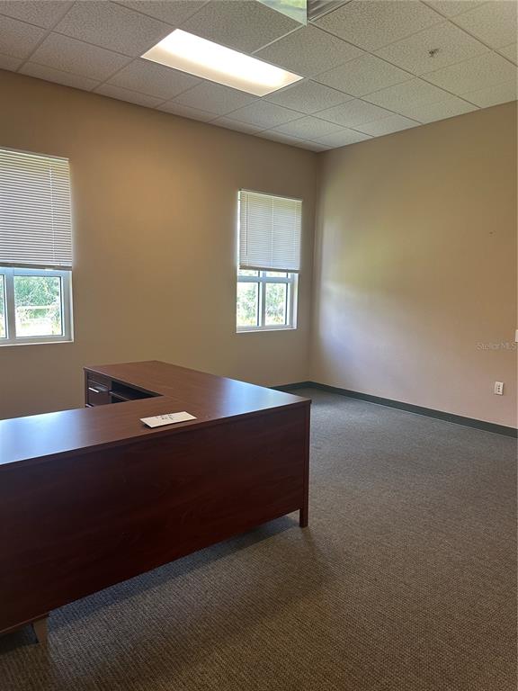 An office space features a large wooden desk, beige walls, carpeted flooring, and two windows — 1611 12TH STREET E UNIT B, PALMETTO, FL