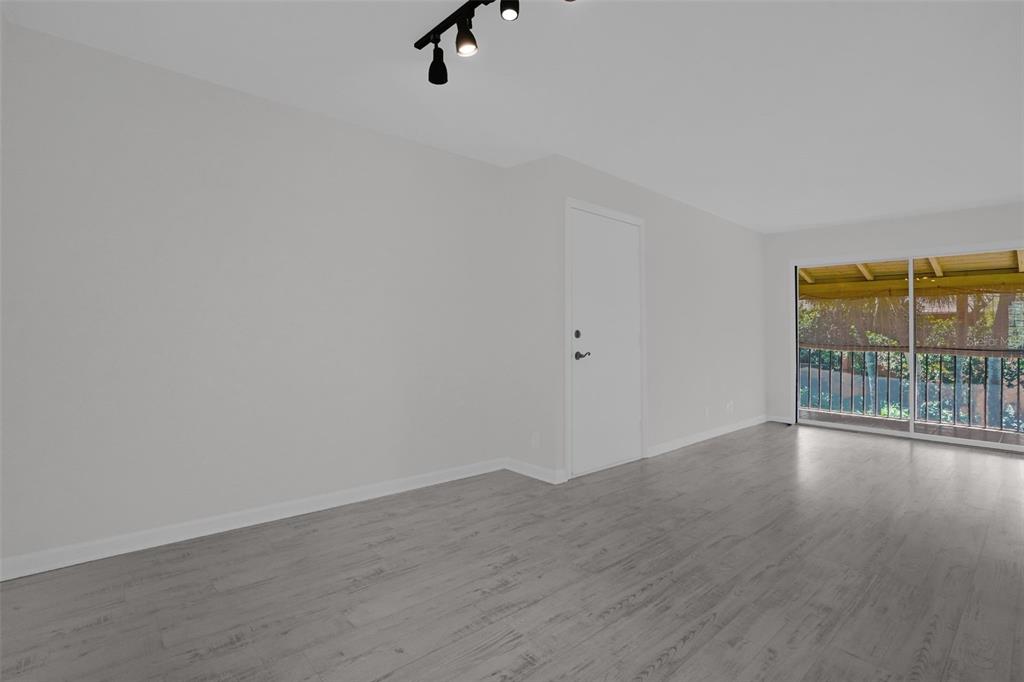 An empty room features light gray wood-look flooring, white walls, track lighting, and a sliding door — 754 E MICHIGAN STREET UNIT 174, ORLANDO, FL