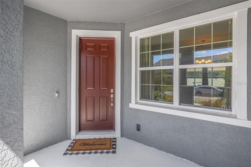 A red front door and a window are set into a gray stucco exterior wall — 5022 AVALON PARK BOULEVARD, WESLEY CHAPEL, FL