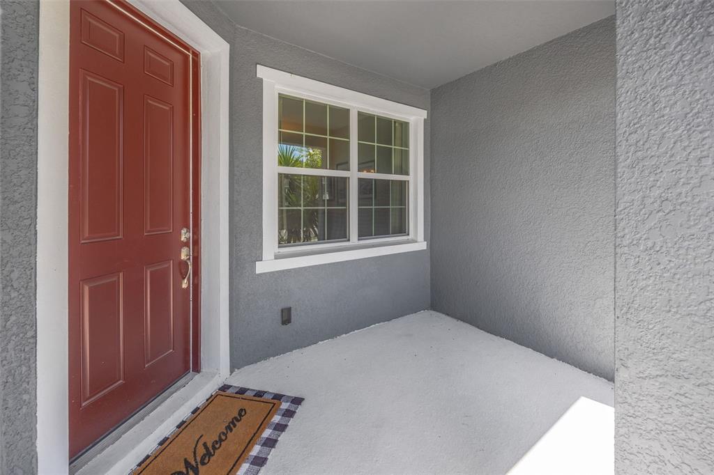 A red front door and a window with white trim face a gray porch — 5022 AVALON PARK BOULEVARD, WESLEY CHAPEL, FL
