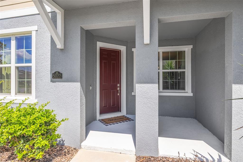The exterior view shows a gray stucco house entrance with a red front door — 5022 AVALON PARK BOULEVARD, WESLEY CHAPEL, FL