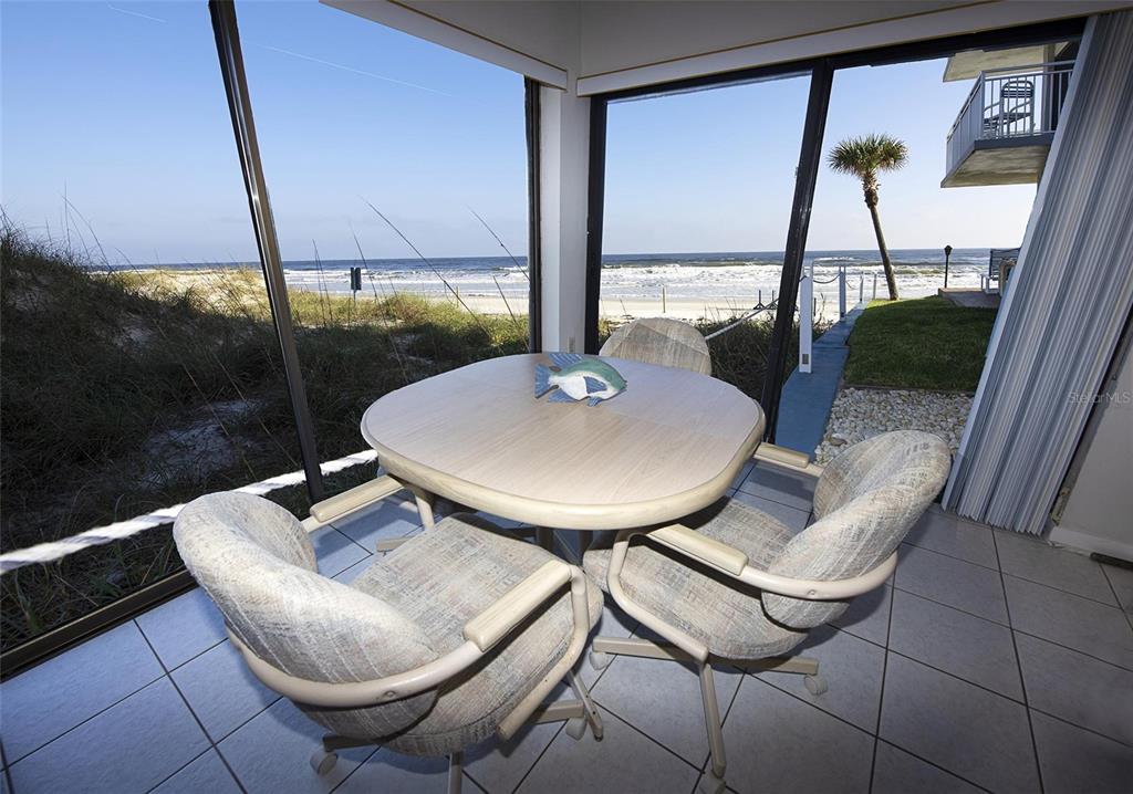 A sunroom features a dining table and chairs overlooking a beach and the ocean — 1571 S ATLANTIC AVENUE UNIT 111, NEW SMYRNA BEACH, FL