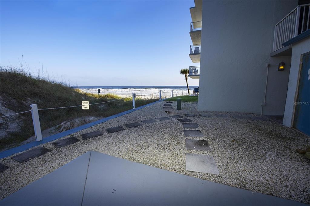 A gravel patio with stone pavers leads to a beach access path beside a building — 1571 S ATLANTIC AVENUE UNIT 111, NEW SMYRNA BEACH, FL