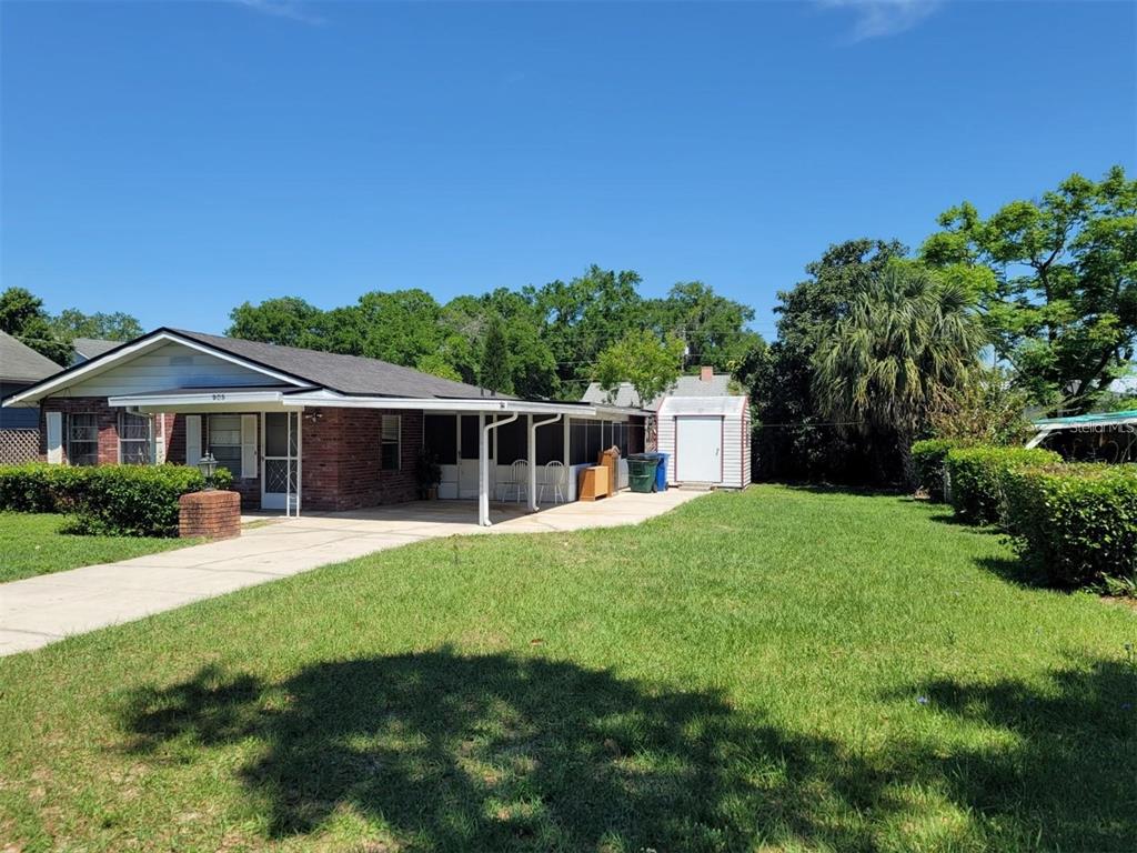 A brick house with a covered patio and a detached shed in a grassy yard — 905 AVENUE E NE, WINTER HAVEN, FL