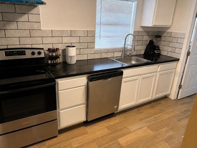 A kitchen features stainless steel appliances, white cabinets, dark countertops, and a subway tile backsplash — 905 AVENUE E NE, WINTER HAVEN, FL