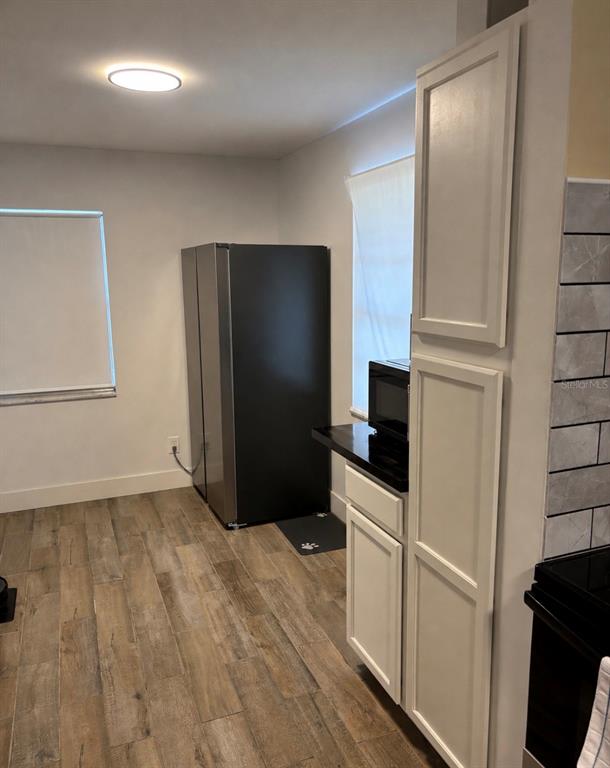 A kitchen features a black refrigerator, white cabinetry, and wood-look tile flooring — 905 AVENUE E NE, WINTER HAVEN, FL