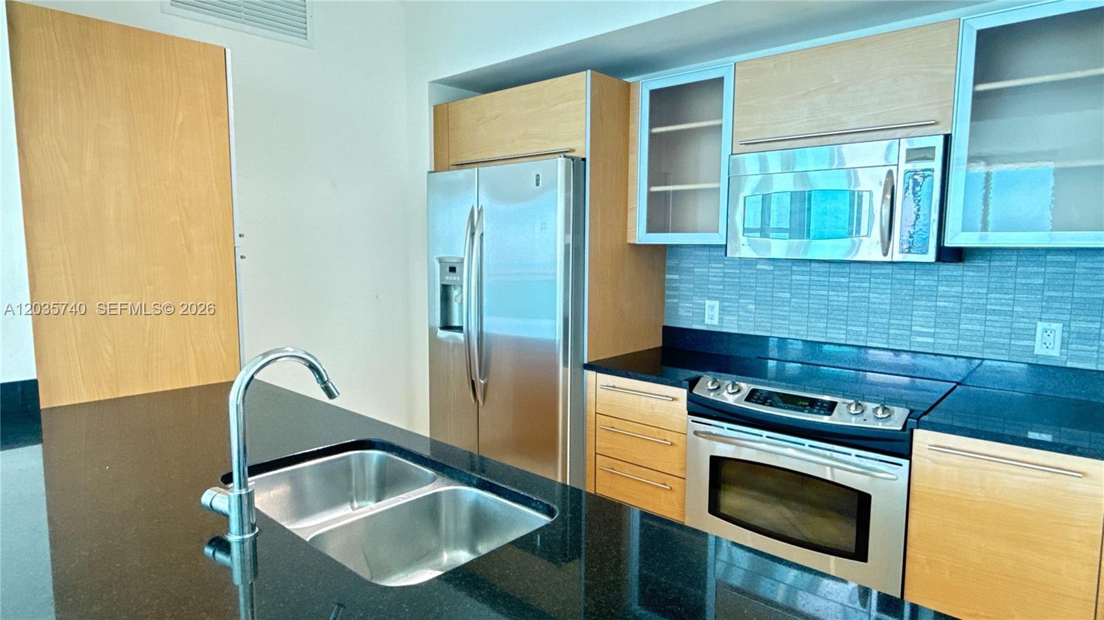 A kitchen features light wood cabinets, black countertops, stainless steel appliances, and a double sink — 950 Brickell Bay Dr # 3411, Miami FL 33131, MIAMI, FL
