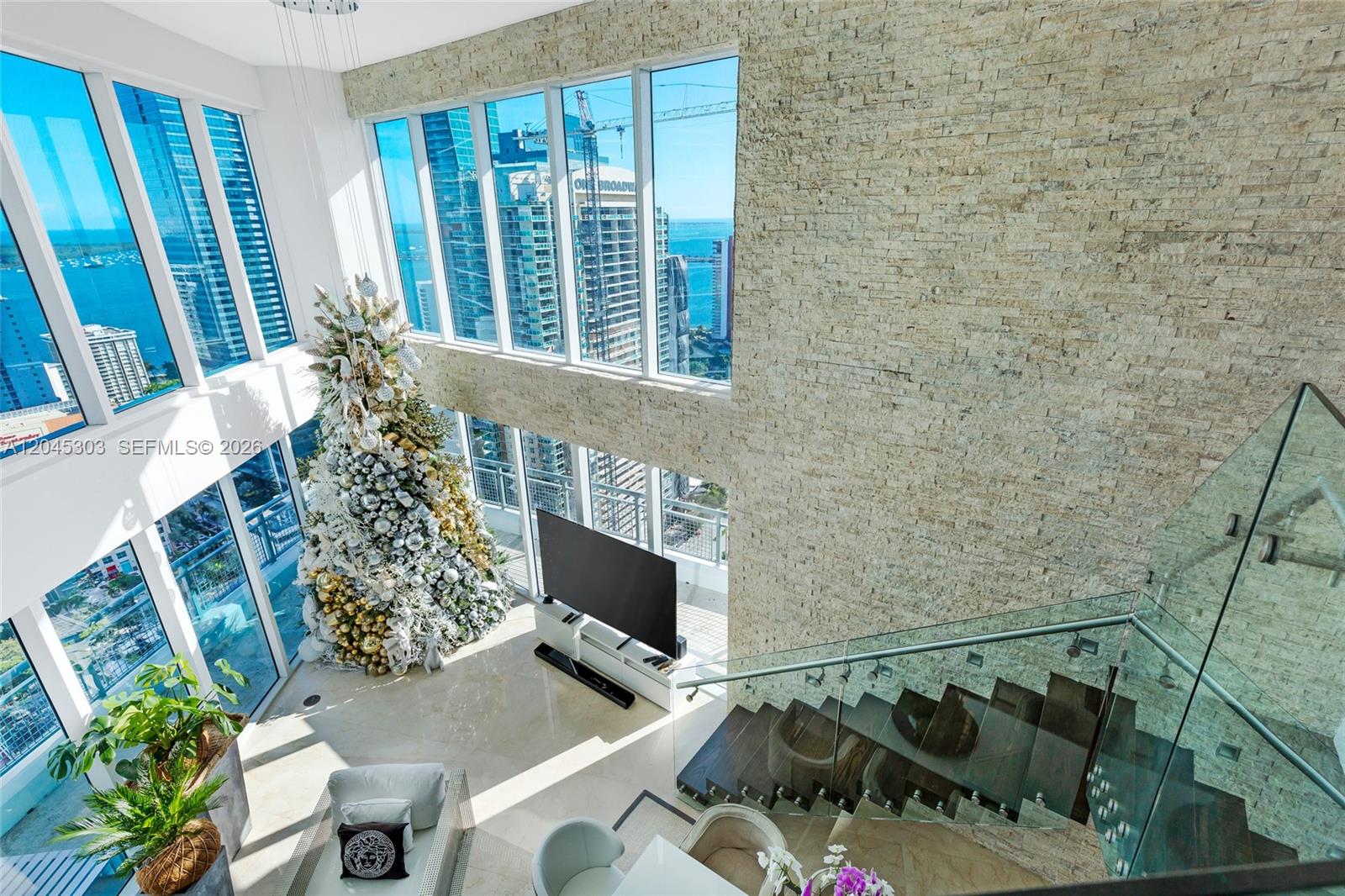 A high-ceiling living room features floor-to-ceiling windows, a stone accent wall, and a staircase — 60 SW 13th St # 3200, Miami FL 33130, MIAMI, FL
