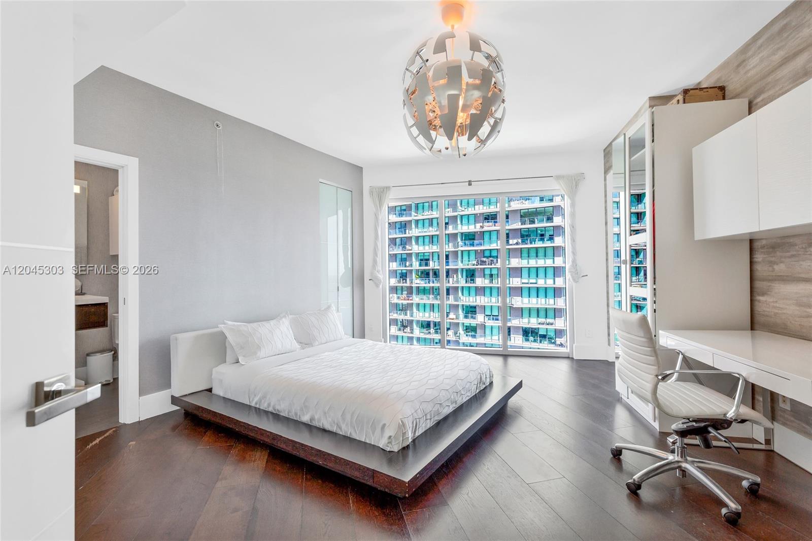 A modern bedroom features a platform bed, a desk, and floor-to-ceiling windows overlooking buildings — 60 SW 13th St # 3200, Miami FL 33130, MIAMI, FL