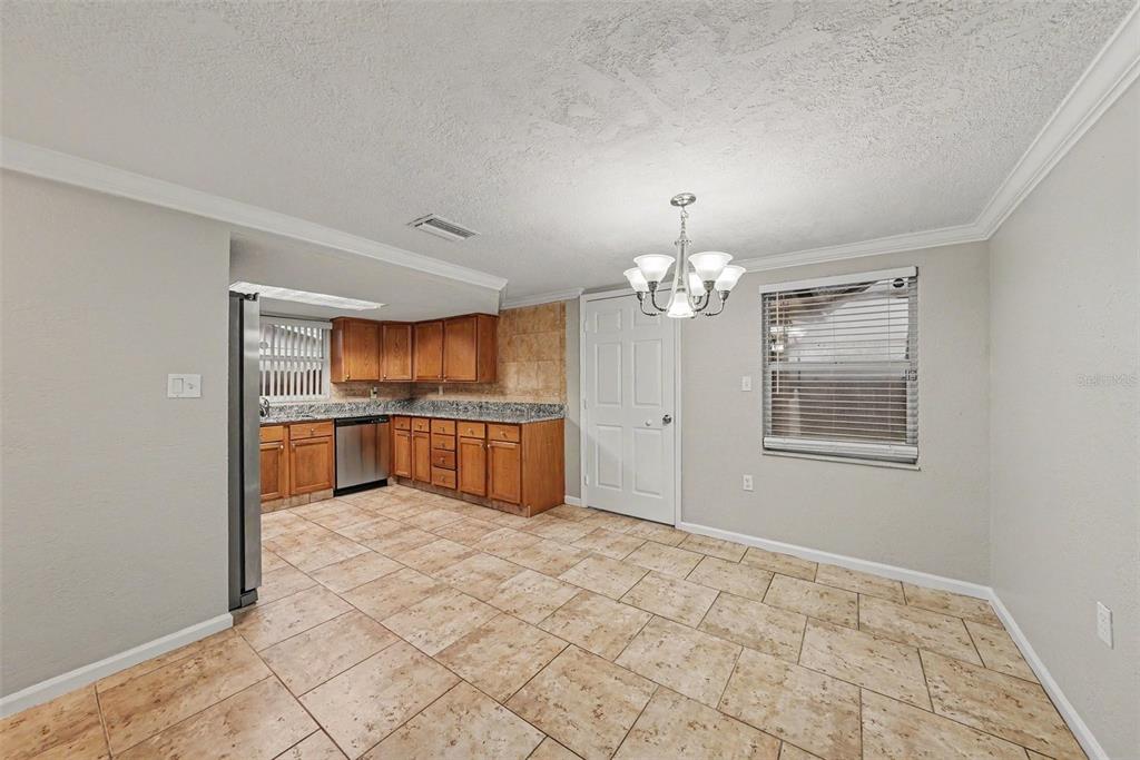 A kitchen and dining area with wood cabinets, tile flooring, and a central chandelier — 9135 HUNT CLUB LANE, PORT RICHEY, FL
