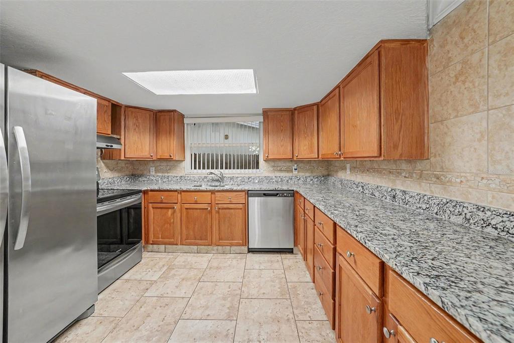 A kitchen features wood cabinets, granite countertops, stainless steel appliances, and tile flooring — 9135 HUNT CLUB LANE, PORT RICHEY, FL