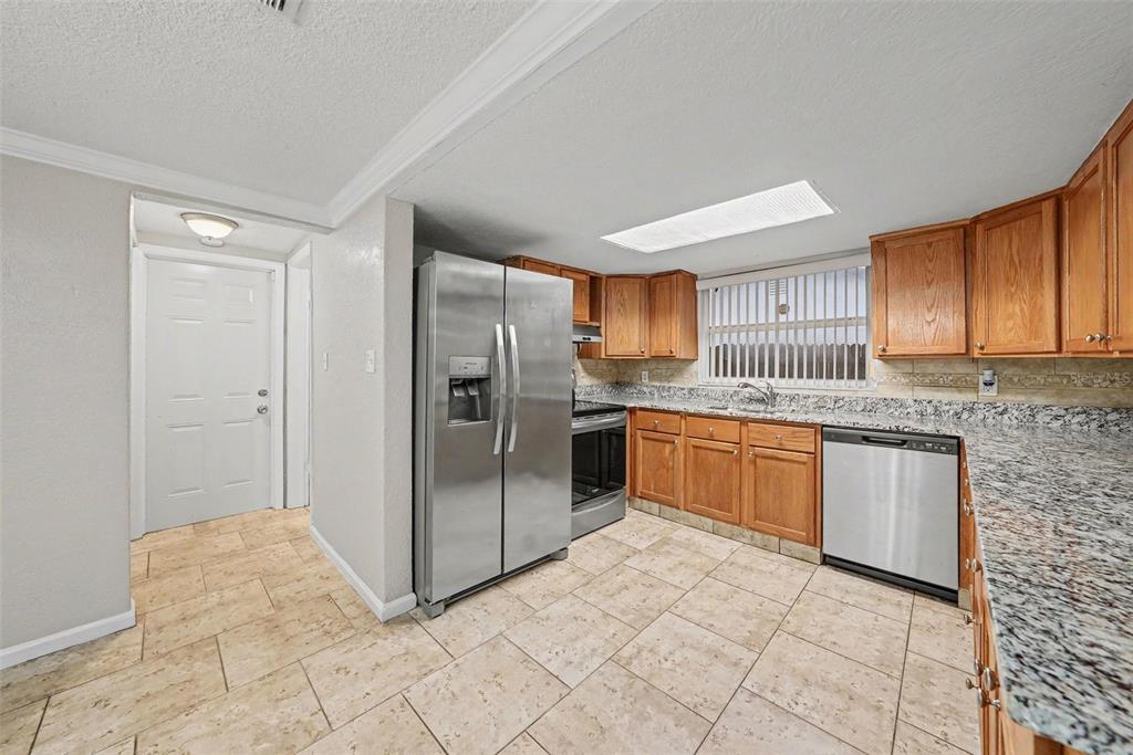 A kitchen features stainless steel appliances, wood cabinets, granite countertops, and light-colored tile flooring — 9135 HUNT CLUB LANE, PORT RICHEY, FL