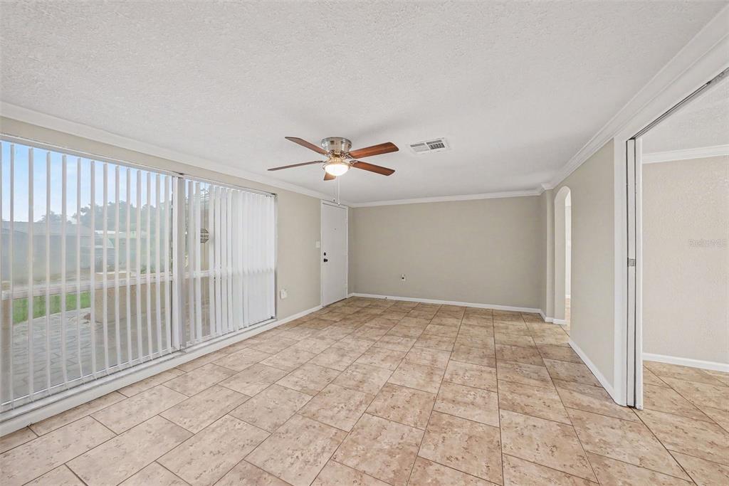 An empty room with tan tile flooring, a ceiling fan, and large vertical window blinds — 9135 HUNT CLUB LANE, PORT RICHEY, FL