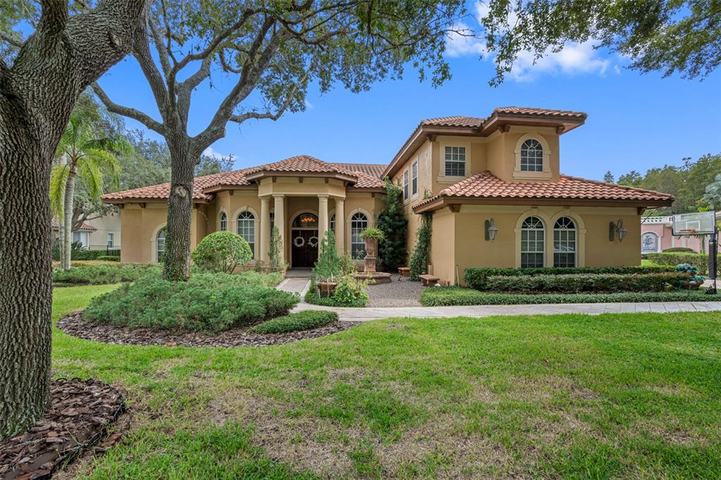 A two-story stucco house with a tile roof and a paved driveway sits behind trees — 531 ISLEWORTH CLOSE, TARPON SPRINGS, FL