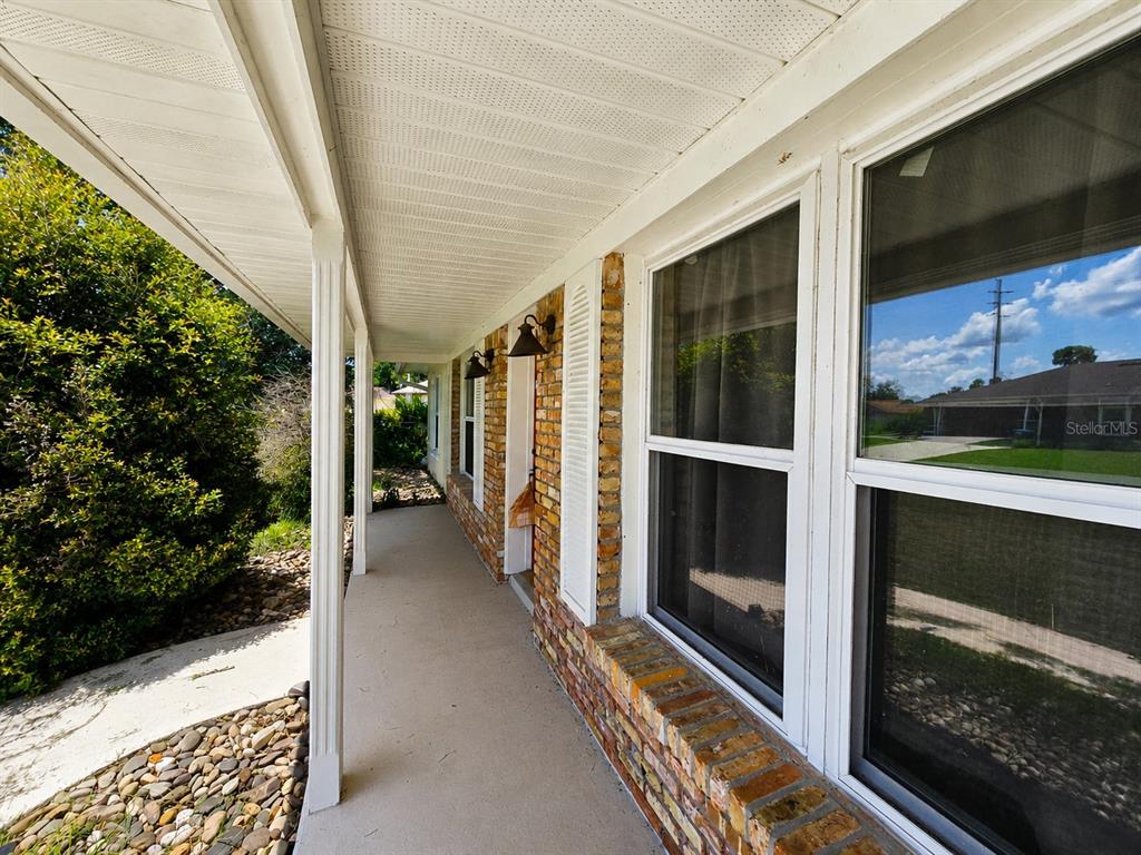 A covered concrete porch runs along the side of a house with brick siding — 1432 LANDOVER AVENUE, DELTONA, FL