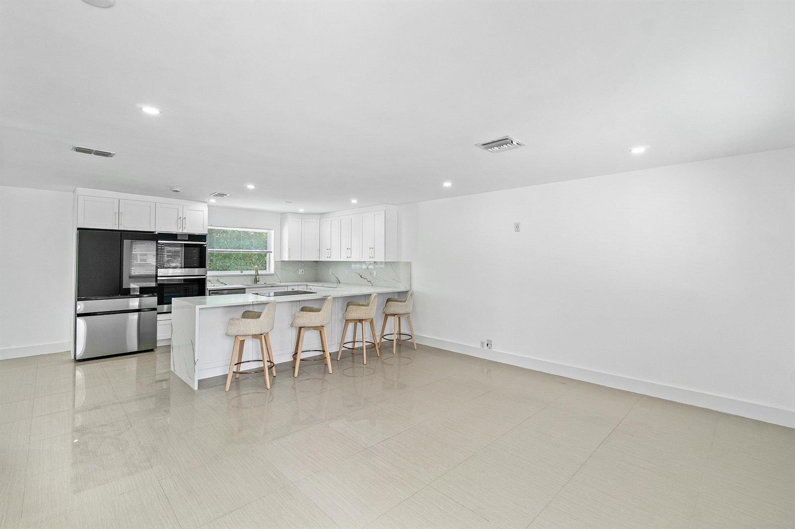 A modern kitchen features white cabinetry, marble-style countertops, stainless steel appliances, and four bar stools — 1531 NW 4th Street, Boca Raton FL 33486, BOCA RATON, FL