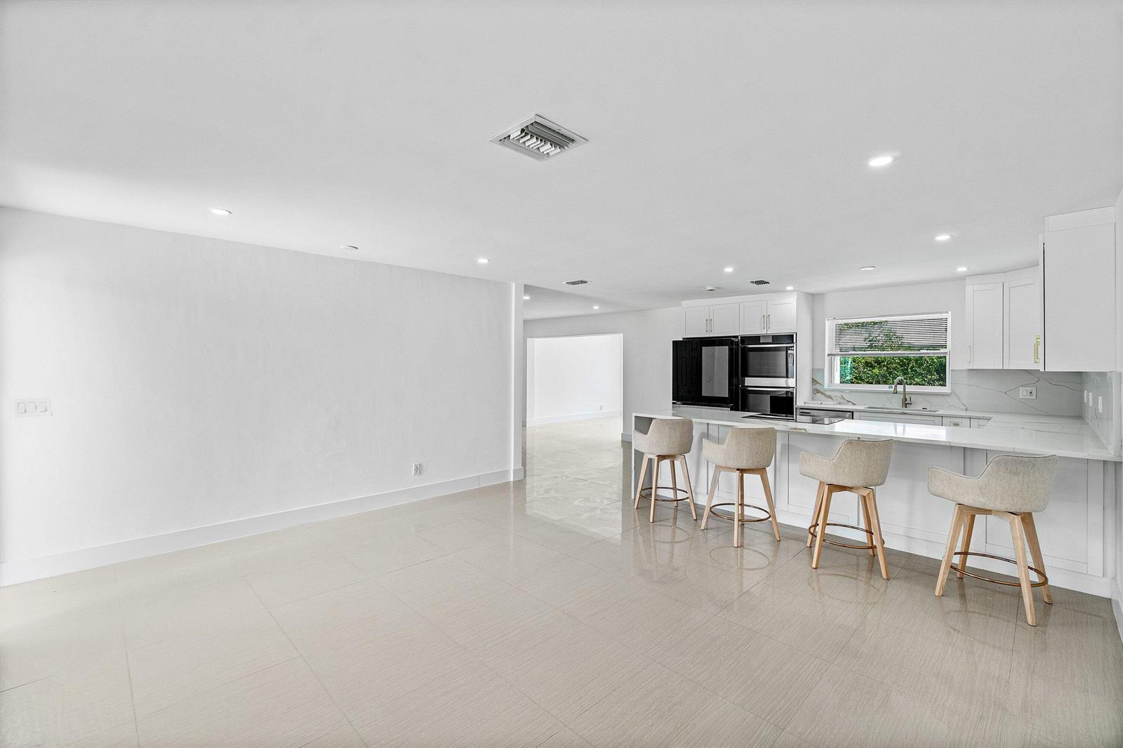 A modern white kitchen features a breakfast bar with four stools and tile flooring — 1531 NW 4th Street, Boca Raton FL 33486, BOCA RATON, FL