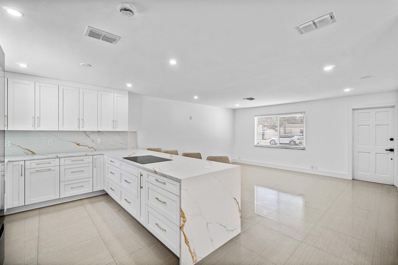 A modern white kitchen features a marble waterfall island, gold hardware, and tile flooring — 1531 NW 4th Street, Boca Raton FL 33486, BOCA RATON, FL