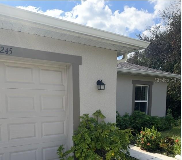 A view of a house exterior showing a garage door, a window, and landscaping — 26245 NORTHERN CROSS ROAD, PUNTA GORDA, FL