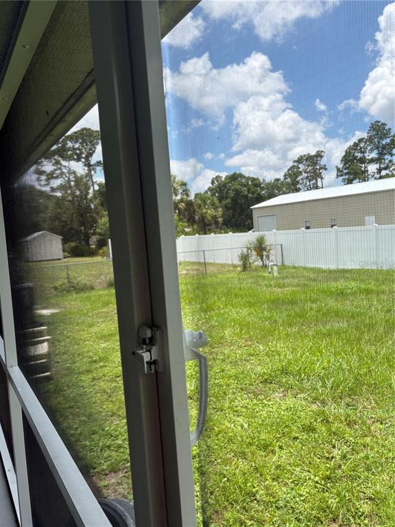A view of a grassy backyard through a screened-in porch door — 2789 RHUMBA TERRACE, NORTH PORT, FL