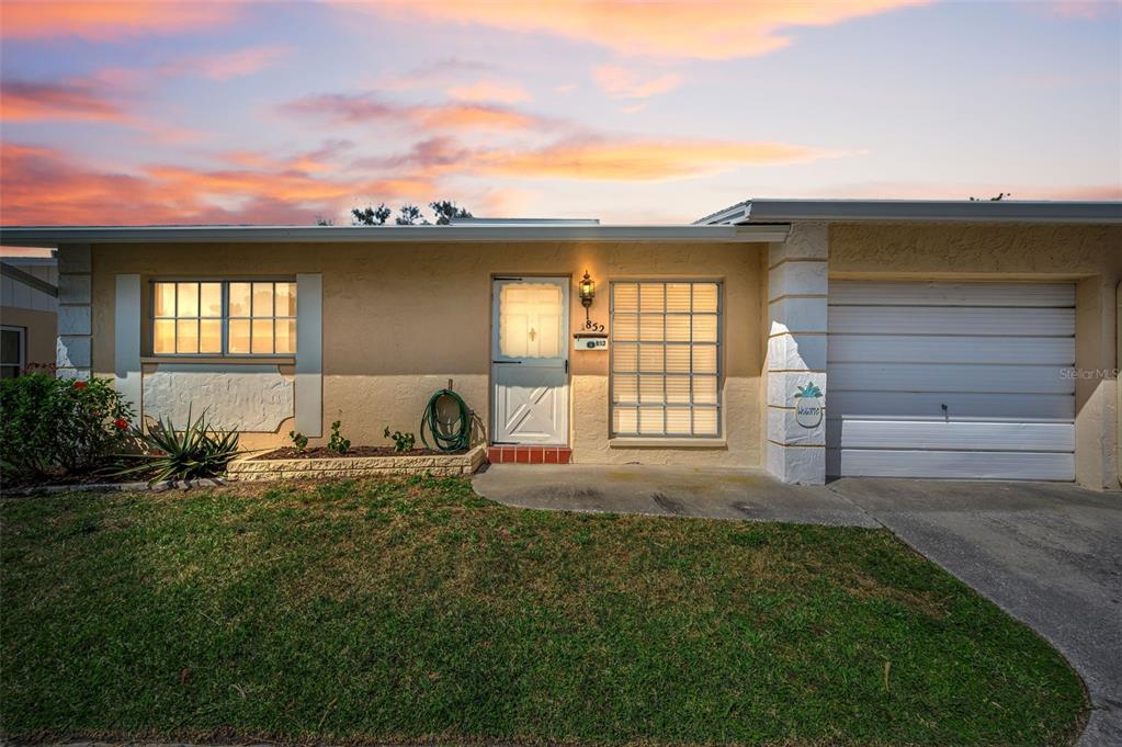 A single-story house with a beige stucco exterior, a garage, and a front lawn — 852 OXFORD COURT, DUNEDIN, FL