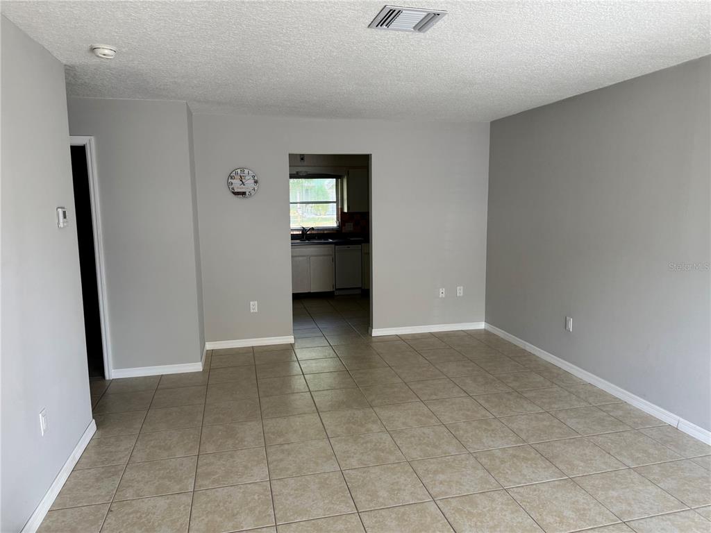 A room with light gray walls, beige tile flooring, and a doorway leading to a kitchen — 852 OXFORD COURT, DUNEDIN, FL