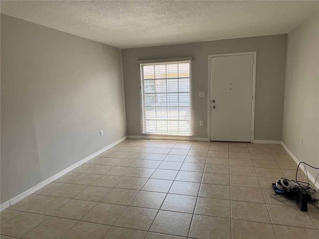 An empty room features light gray walls, beige tile flooring, a window, and a door — 852 OXFORD COURT, DUNEDIN, FL